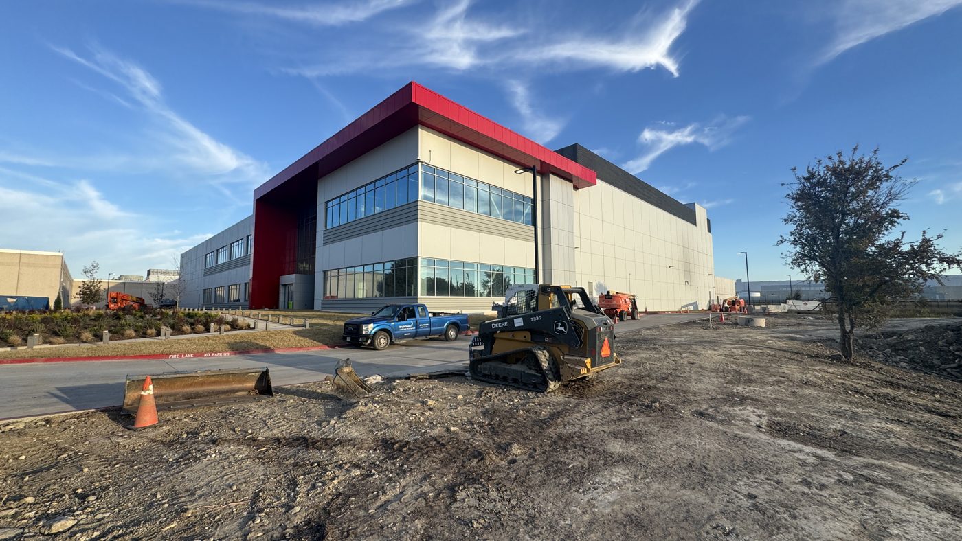 QTS hyperscale data center campus under construction in Fort Worth, Texas, with a red entry canopy and glass curtain-wall office