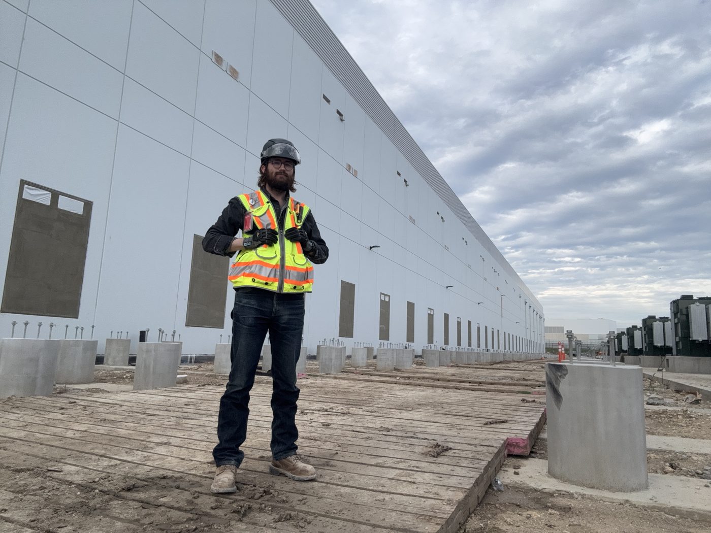 Founder Richard Batson in safety gear on an active large-scale construction site, a long tilt-wall building behind him